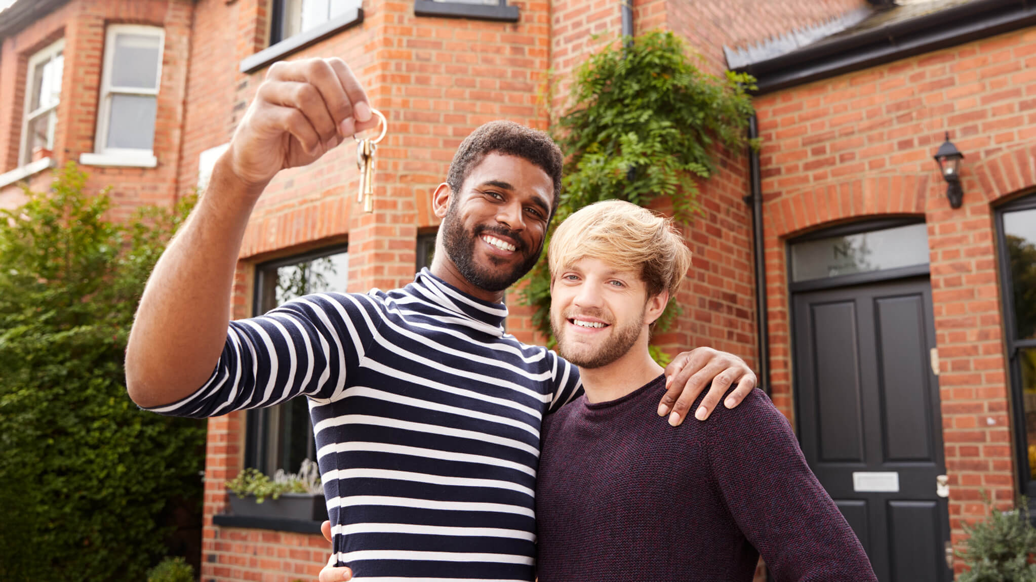 Male couple holding up keys to townhouse