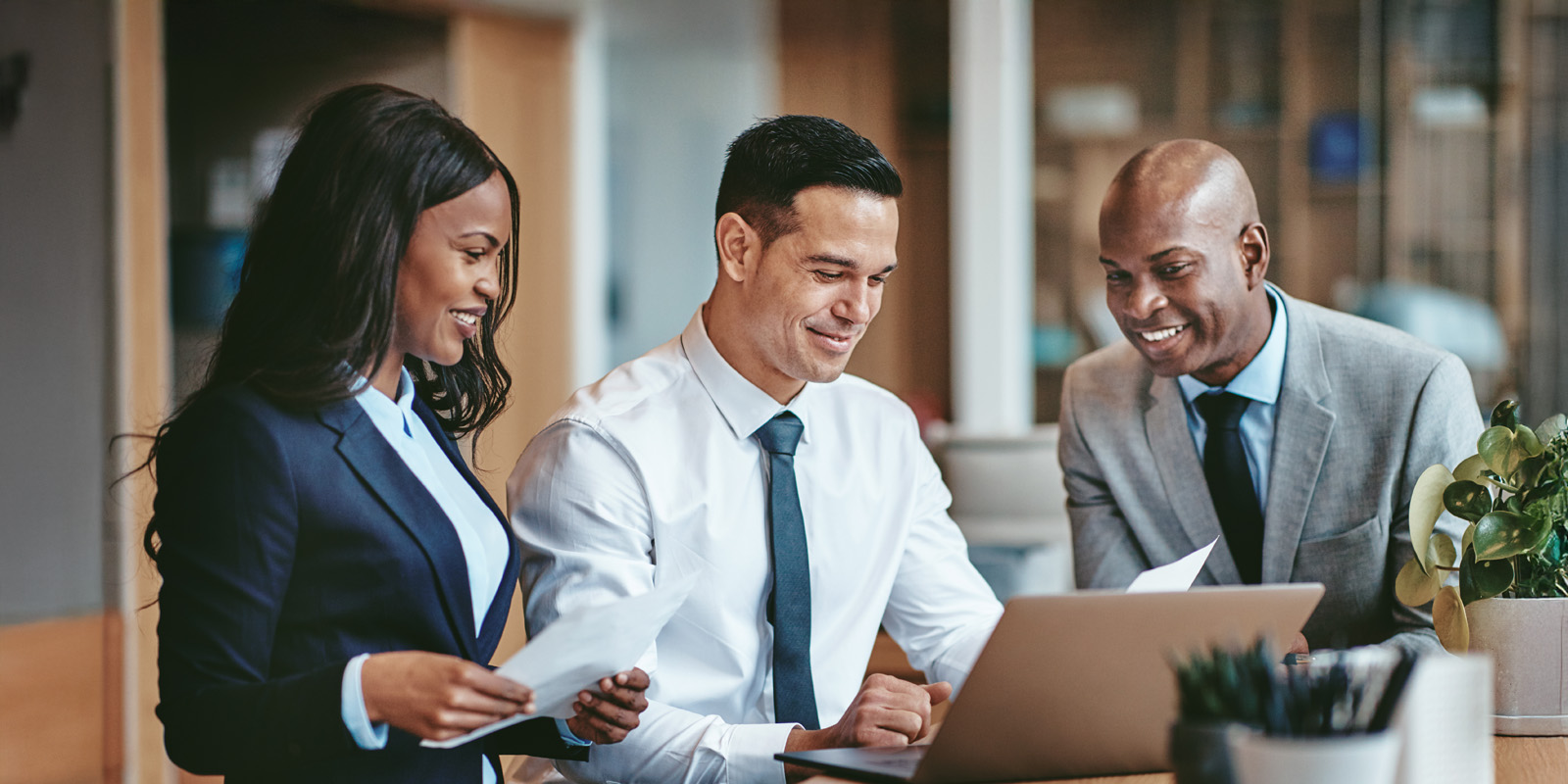 Black woman and black man leaning in to look at white mans laptop screen